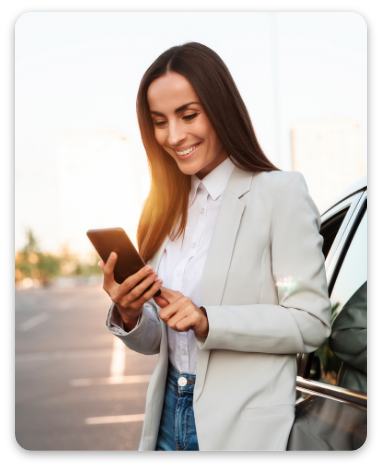 Successful smiling woman in formal smart wear is using her smart phone while standing near modern car outdoors