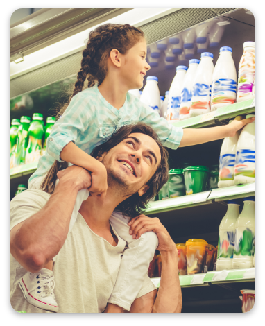 Beautiful young parents and their cute little daughter are smiling while choosing food in the supermarket. Girl is sitting on her dad's shoulders